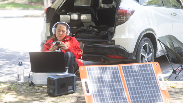 A car camper with headphones using devices while charging a solar panel.