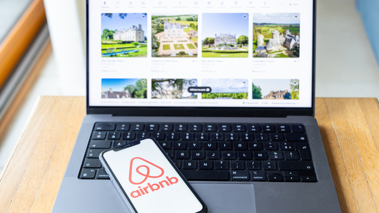 A smartphone with the Airbnb app sitting on a laptop checking available listings.