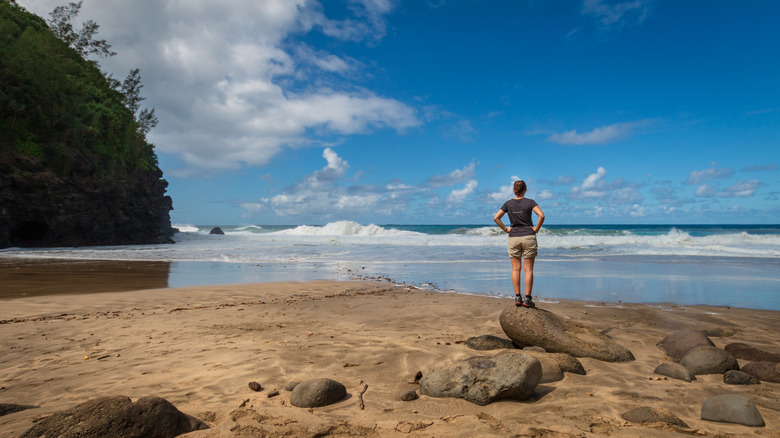 a woman standing on a boulder looking out to sea