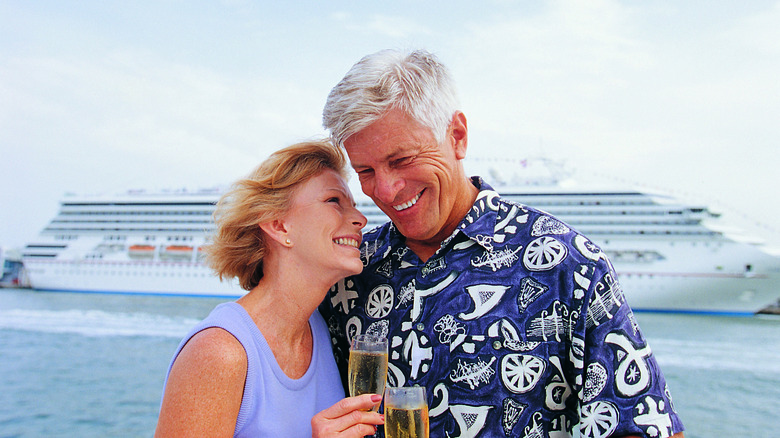 A senior couple clinks champagne in front of a cruise ship