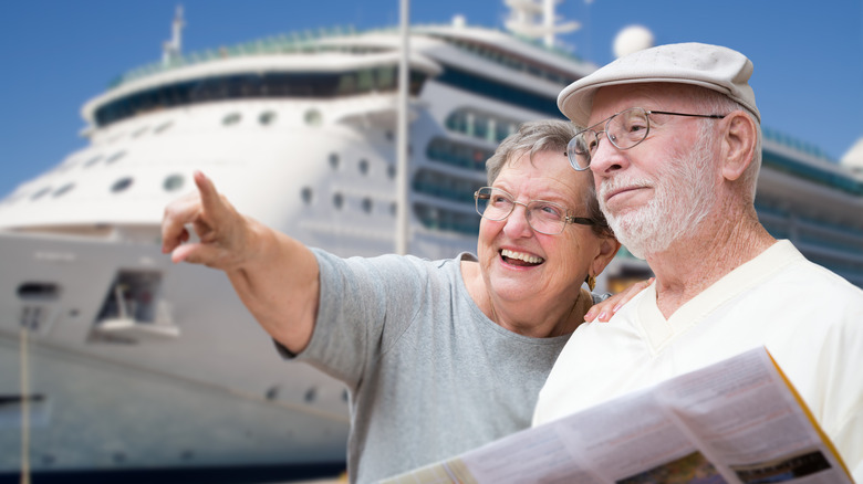 A senior couple looks into the distance in front of a cruise ship