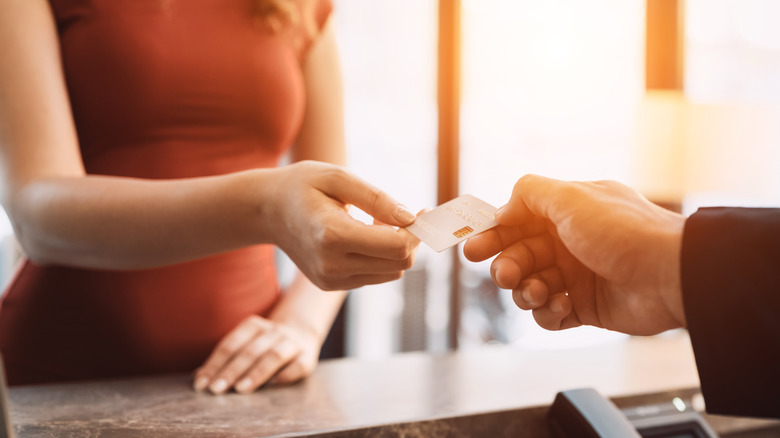 A person handing a credit card across a hotel desk and to an employee to pay for a room
