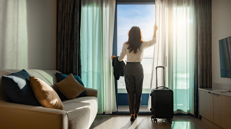 A woman opening the curtains in her hotel room.