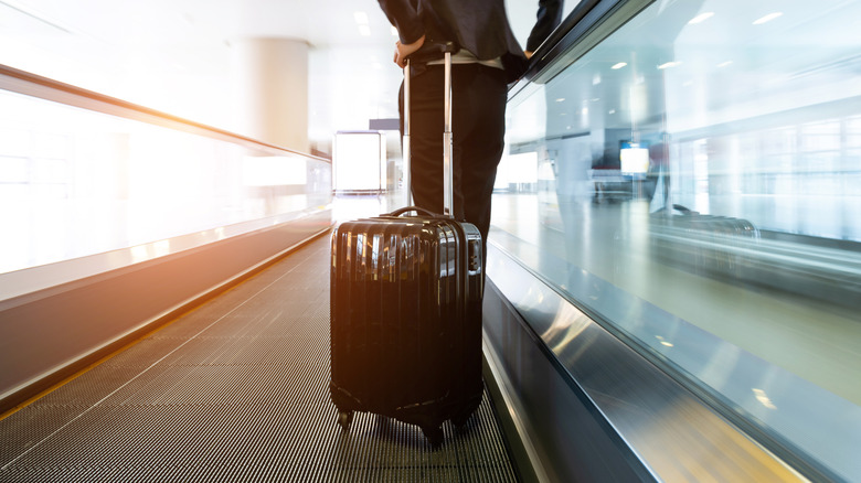 Traveler standing on airport walkway with roller suitcsase