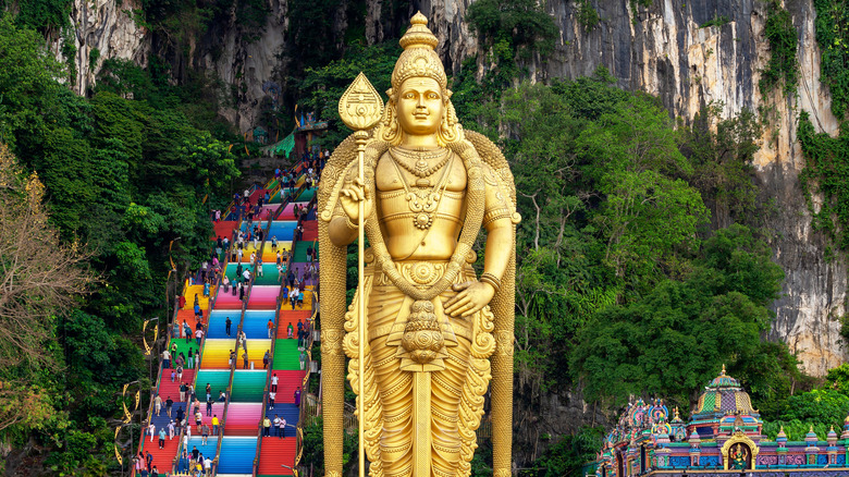 A large golden statue with colorful stairs leading to cave