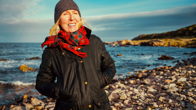 A woman in a waxed jacket stands on a rocky beach