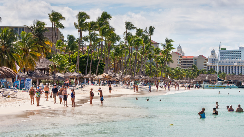 a crowded beach with palm trees and tall buildings