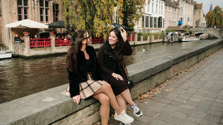 Two women in coats talk on edge of Belgium canal