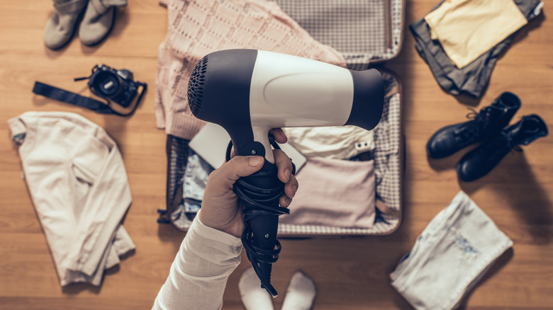 Hand holding hair dryer over suitcase