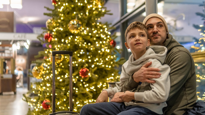 Man and child sitting by Christmas tree at airport