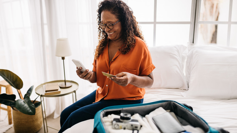 Woman sitting on bed smiling looking at phone and holding debit card