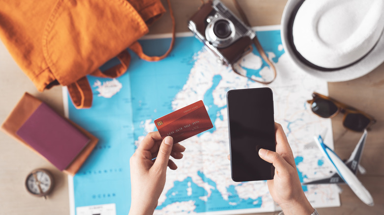 Hands holding a phone & credit card over travel items
