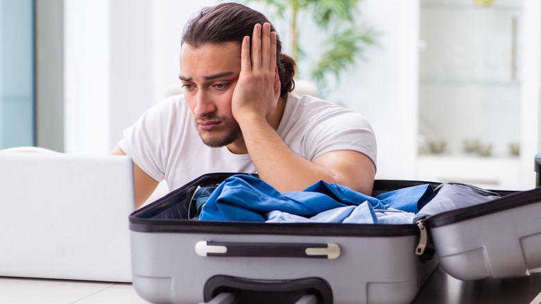 man with half-packed suitcase on laptop