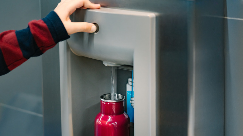 Person filling water bottle at airport water dispenser