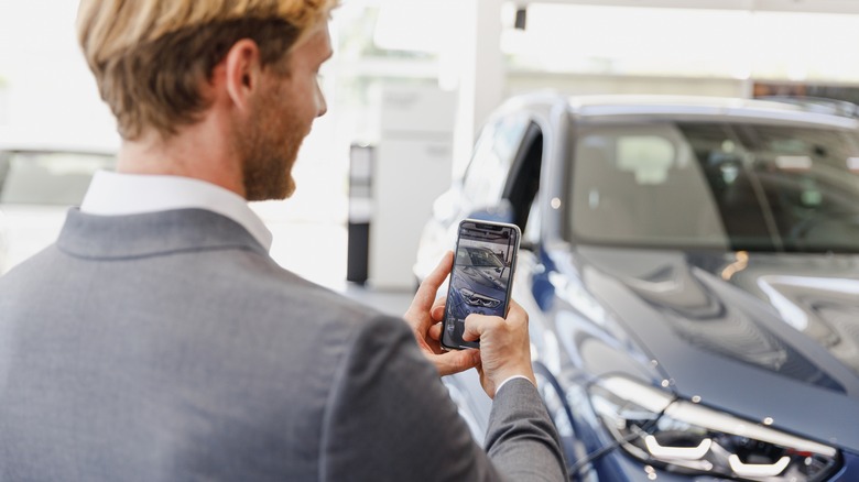 A man taking a photo of a car in a garage with his smart phone.