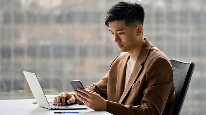 man looking at his phone and laptop