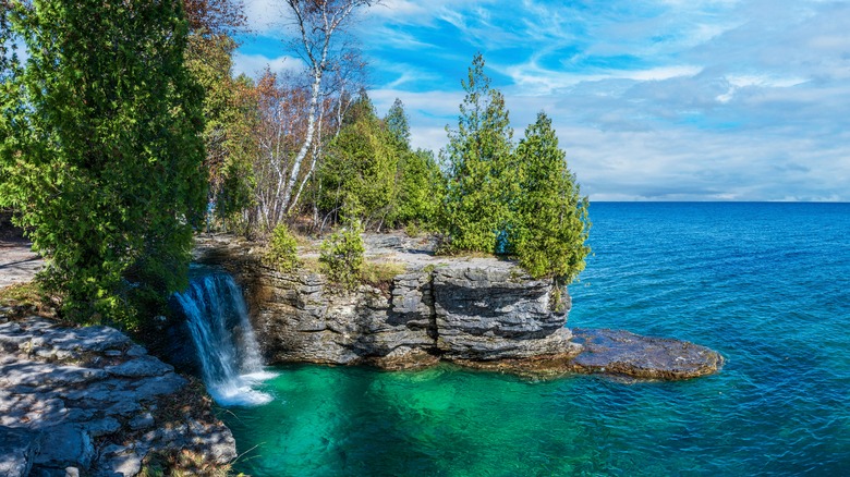 A treelined limestone cliff above a crystal blue large lake
