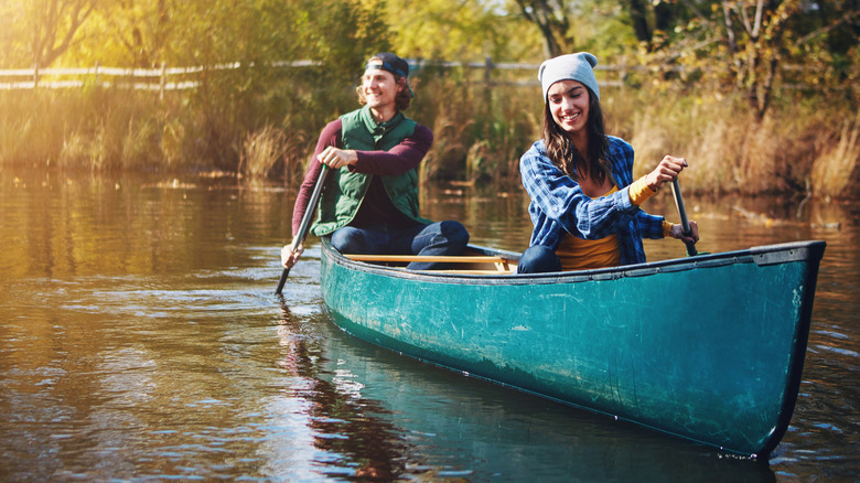 A couple dressed for autumn canoeing a calm river in evening light