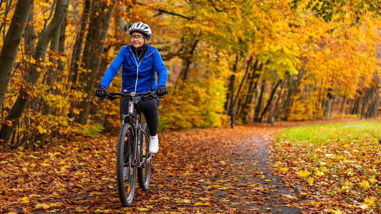 A middle-aged woman biking a forest trail covered in autumn leaves