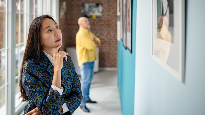 Two visitors view art pieces in a brightly lit gallery, showcasing modern artwork.