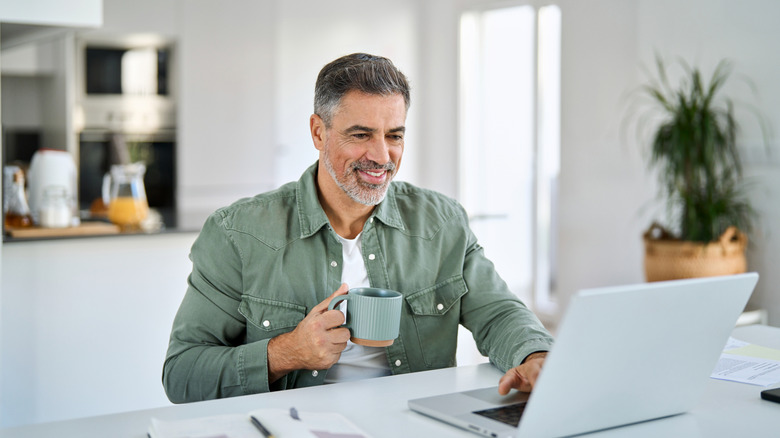 grey-haired man on laptop having coffee