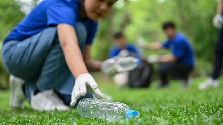 Volunteers picking up trash at a park with one person in the foreground picking up an empty plastic bottle