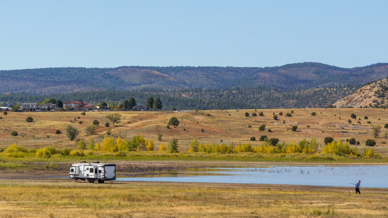 An RV park by a shallow lake surrounded by yellow scrub and brush at Storrie Lake State Park in Las Vegas, New Mexico