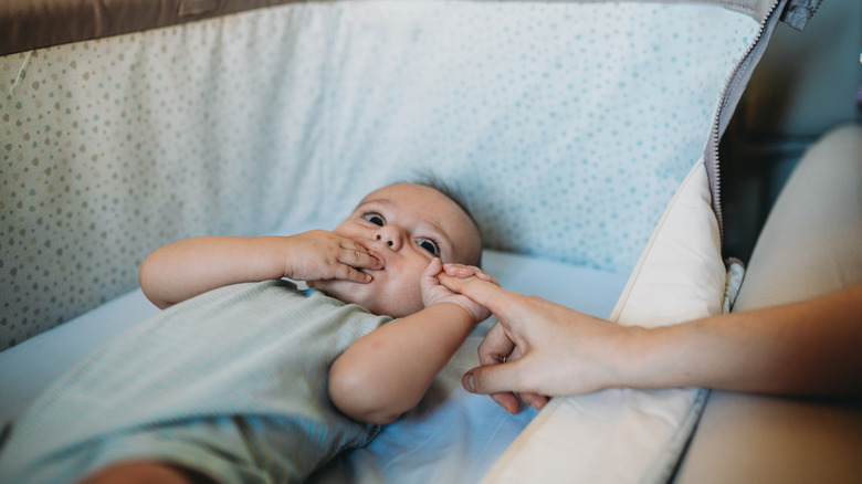Mother reaching out to baby lying down in crib