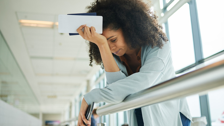 Women stressed at airport holding boarding pass and phone in airport line