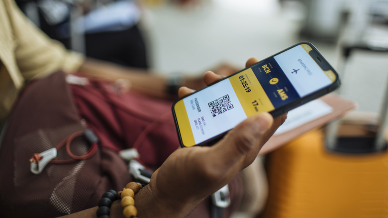 Man checking yellow and blue boarding pass on his phone from bcn to ams
