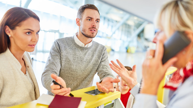 Stressed couple speaking to airport gate agent on phone